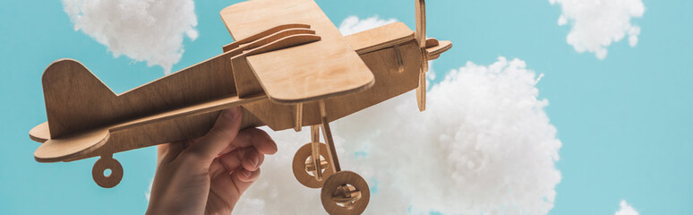 wooden toy plane flying among white fluffy clouds made of cotton wool isolated on blue, panoramic shot