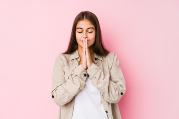 Young caucasian woman posing in a pink background holding hands in pray near mouth, feels confident.