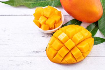 Fresh mango,beautiful chopped fruit with green leaves on bright wooden table background. Tropical fruit design concept, close up, copy space.