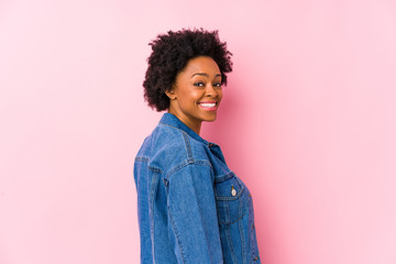 Young african american woman against a pink backgroound isolated looks aside smiling, cheerful and pleasant.