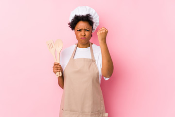 Young african american cook woman showing fist to camera, aggressive facial expression.