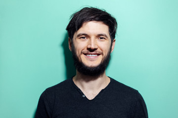 Studio portrait of young smiling bearded man with disheveled hair on background of aqua menthe color.