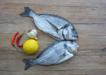 Raw dorado or sea bream fish on wooden table with vegetables, top view. 