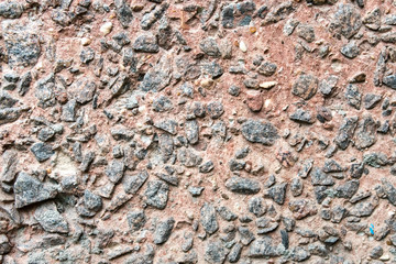 Red concrete wall covered by small black rocks.