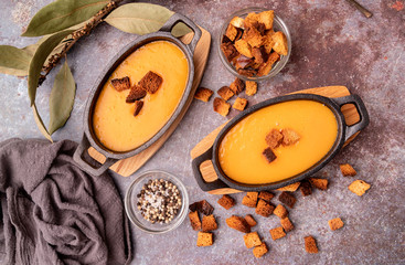 Fototapeta premium Pumpkin soup with croutons in iron pots decorated with croutons, laurel leaves and spices top view on dark background