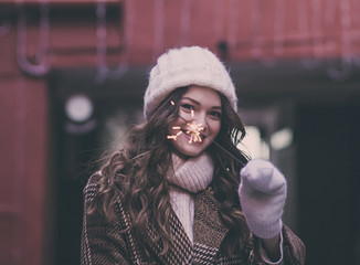  portrait of a smiling beautiful woman in winter clothes with a sparkler on the street at christmas