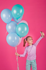 Fototapeta na wymiar happy little girl with balloons on a pink background taking pictures of herself on her phone