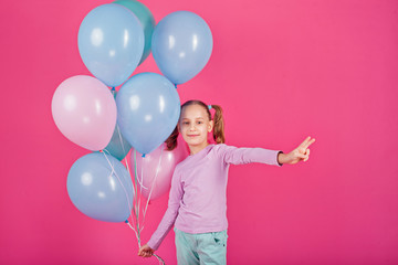 happy little girl with balloons on pink background shows hand sign