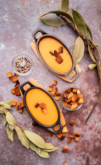 Pumpkin soup with croutons in iron pots decorated with croutons, laurel leaves and spices top view on dark background