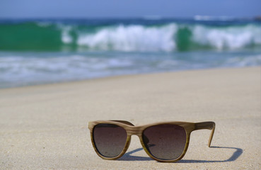 Fototapeta na wymiar Sunglasses on the beach with blurry splashing waves in background