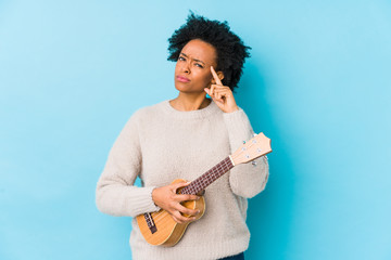 Young african american woman playing ukelele isolated pointing temple with finger, thinking, focused on a task.