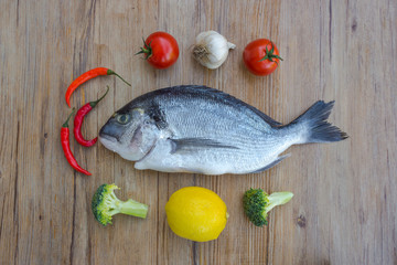 Raw dorado or sea bream fish on wooden table with vegetables, top view. 