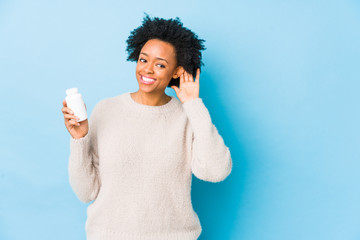 Middle age african american woman holding a vitamin bottle trying to listening a gossip.