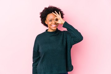 Middle aged african american woman against a pink background isolated excited keeping ok gesture on eye.