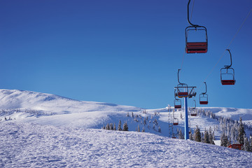 Ski lift with seats going over the mountain and paths from skies and snowboards.