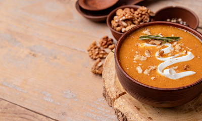 Obraz na płótnie Canvas Pumpkin soup with creme in brown bowl decorated with walnuts with copy space on wooden background