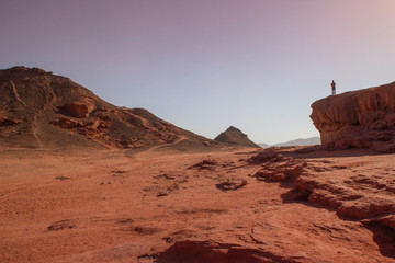 A Caucasian male traveler climbed a rock and stands against the sky in Timna National Park, Israel,
