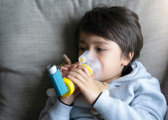 Poor boy tired from chest coughing holding inhaler mask, Child closing his eyes while using the...