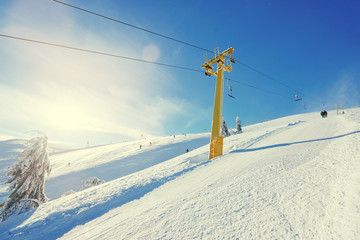 Ski lift going over the snowy mountain and paths from skies and snowboards.