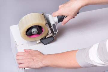 Obraz na płótnie Canvas Worker works with tape dispenser, closing cardboard industrial box