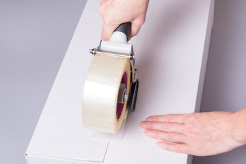 Worker works with tape dispenser, closing cardboard industrial box