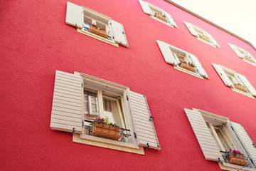 Red house wall with white windows with shutters.