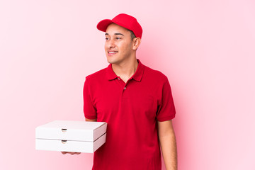 Young pizza delivery latin man isolated looks aside smiling, cheerful and pleasant.