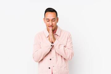 Young latin man posing isolated holding hands in pray near mouth, feels confident.