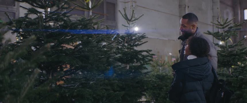 African American black couple looking for a perfect Christmas tree together at tree vendor. Shot on ARRI Alexa Mini w/ Atlas Orion 2x Anamorphic lenses