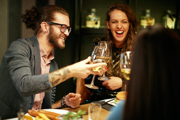 Cheerful group of friends sitting in restaurant for dinner and toasting with white wine.