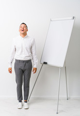 Young latin coaching man with a whiteboard isolated relaxed and happy laughing, neck stretched showing teeth.