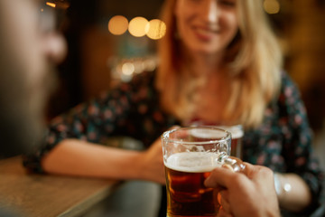 Close up of couple toasting with beer while standing at pub.