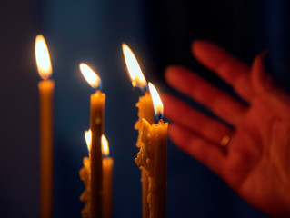 Burning in the dim light of candles in the Christian Church. In the background, a woman's hand.