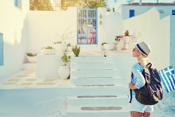 Young traveling woman in hat with rucksack and national greek flag walking on old town enjoying the view.