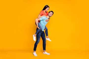 Fototapeta na wymiar Full body photo of two funny people guy carrying lady piggyback meet summer adventures together wear casual trendy blue orange t-shirts jeans isolated yellow color background