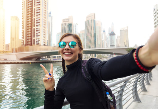 Pretty young woman tourist takes selfie portrait at Dubai fountain,Burj Khalifa. Beautiful female student takes photo for travel blog.