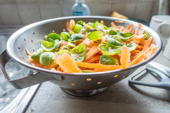 Sprout and carrot vegetable peelings in a metal colander in a residential kitchen as part of preparing a meal.