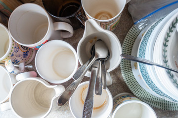 Dirty cups, mugs, plates and cutlery at the side of a kitchen sink waiting to be cleaned and washed up.