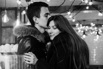 Cute smiling couple in love standing in a cafe hugging each other, image through the glass