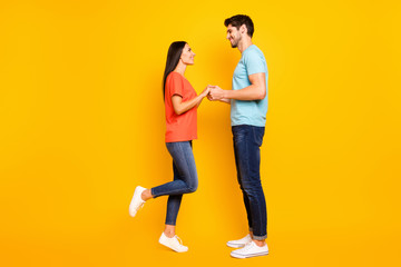 Will you marry me. Full body photo of two cute people couple guy lady hold arms look eyes love declaration wear casual blue orange t-shirts jeans isolated yellow color background