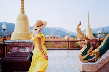 Travel by Asia. Young woman in hat and yellow dress walking near the Chalong buddhist temple on Phuket Island in Thailand. - obrazy, fototapety, plakaty