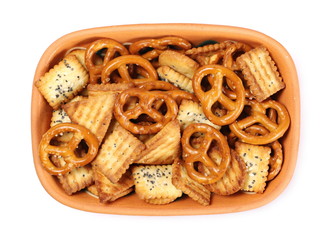 Salty cracker and pretzel snacks, party mix in clay bowl isolated on white background, top view