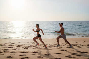 Healthy lifestyle. Jogging outdoors. Young man and woman is running on the sand beach.