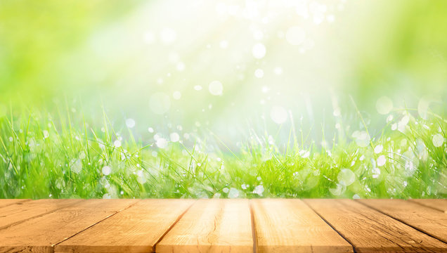 Beautiful spring natural  background with green fresh juicy young grass and empty wooden table in nature morning outdoor.  Beauty bokeh and sunlight.