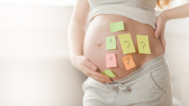Concept of choosing baby name. cropped shot of pregnant woman with question marks on paper stickers on tummy,