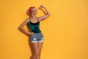 Strong and energy. Pretty young  woman showing bicep on her arm. Colorful portrait with yellow background.