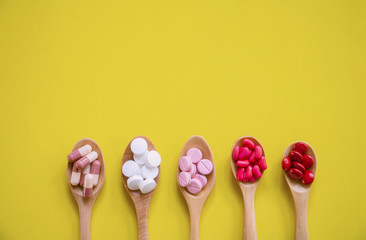 Top view Medicine on wood spoon.Assorted pharmaceutical red capsules with Multi color vitamins and supplements.They are on Yellow background and copy space.Photo concept healthy and medication.