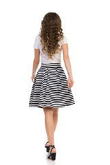 Young Woman In Striped Skirt And High Heels Is Walking. Rear View.