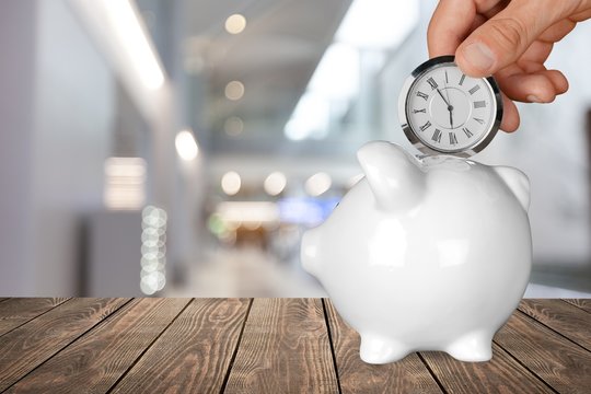Hand depositing  clock  in the piggy bank on background