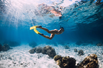 Freediver girl with fins glides over sandy bottom in blue ocean - obrazy, fototapety, plakaty